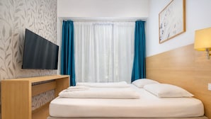 Habitación de hotel con cama, televisión, cabecero de madera, escritorio y lámpara.
