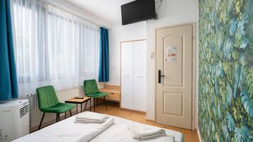 Hotelkamer met een bed, twee groene stoelen, een bureau, een radiator, een aan de muur bevestigde televisie en een deur met een bordje.