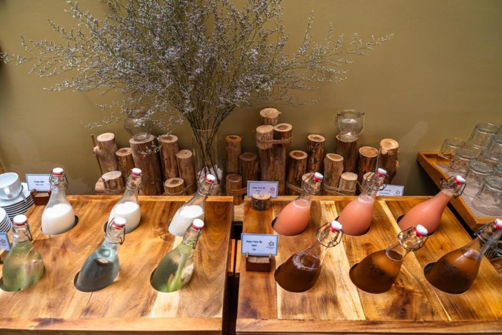 A display of various bottles and glasses on wooden shelves, with a decorative arrangement of branches and vases in the background.
