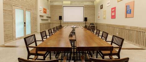 A conference room with a long wooden table, chairs, a projector screen, and a whiteboard.