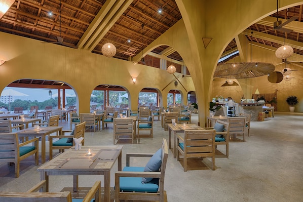 A spacious restaurant with wooden tables and chairs, large windows, and a high ceiling with exposed beams.
