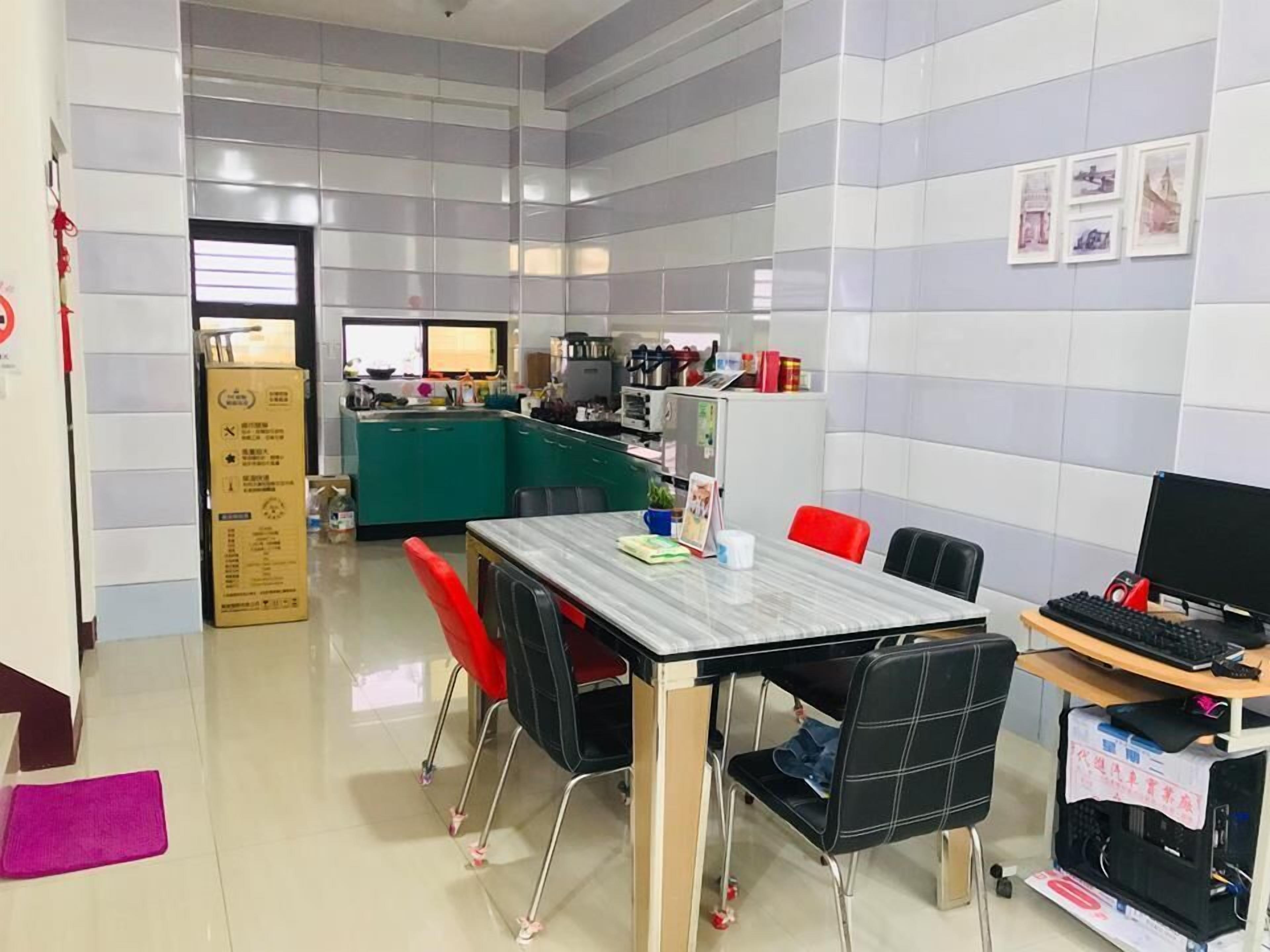 A modern kitchen with a dining area, including a table with chairs, a computer setup, and a refrigerator.