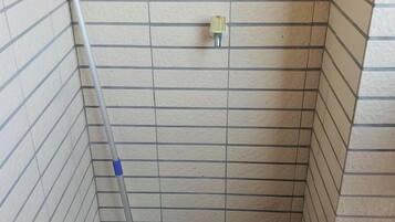 A small, tiled bathroom with a shower area, a mop leaning against the wall, and a white bottle on the floor.