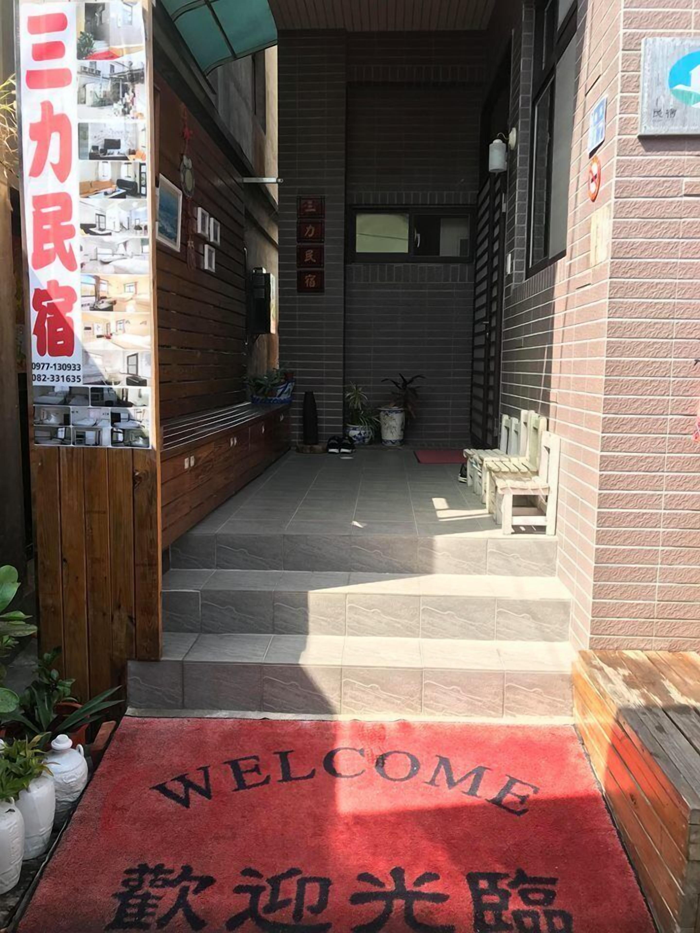 Entrada de hotel con alfombra roja, cartel de bienvenida y tablón anunciando habitaciones.