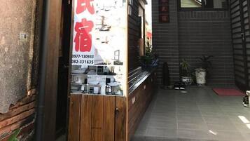 A narrow alleyway with a wooden fence on one side and a building entrance on the other. A vertical sign with red text is visible, indicating a business or service.