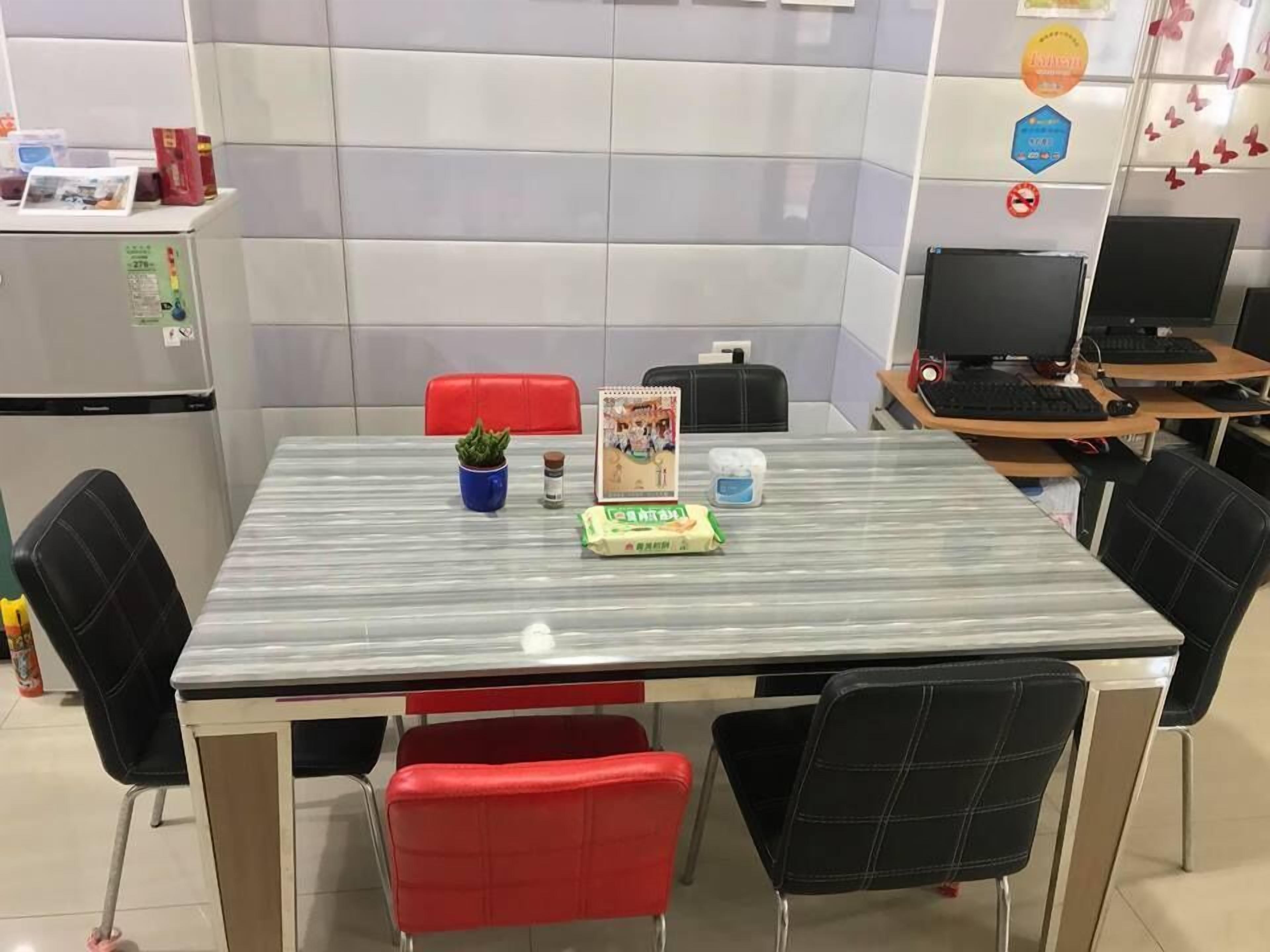 Una sala de conferencias con una mesa de vidrio, sillas rojas y negras, una pequeña planta en maceta, un cuaderno y un ordenador.