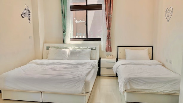 A hotel room with two single beds, a nightstand, a window with curtains, and a wall decal. - Sanli B&B (Jinhu)