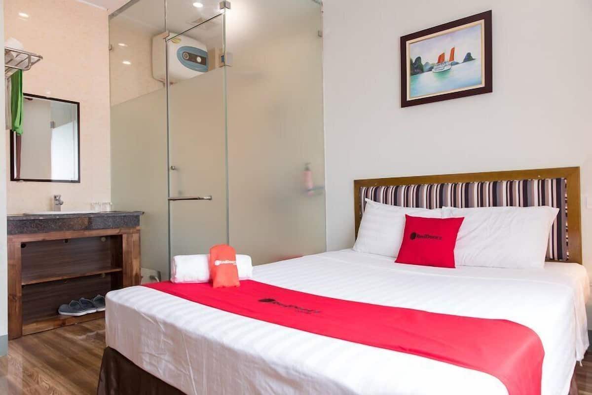 Habitación de hotel con cama, ducha, tocador con espejo y un cuadro en la pared.