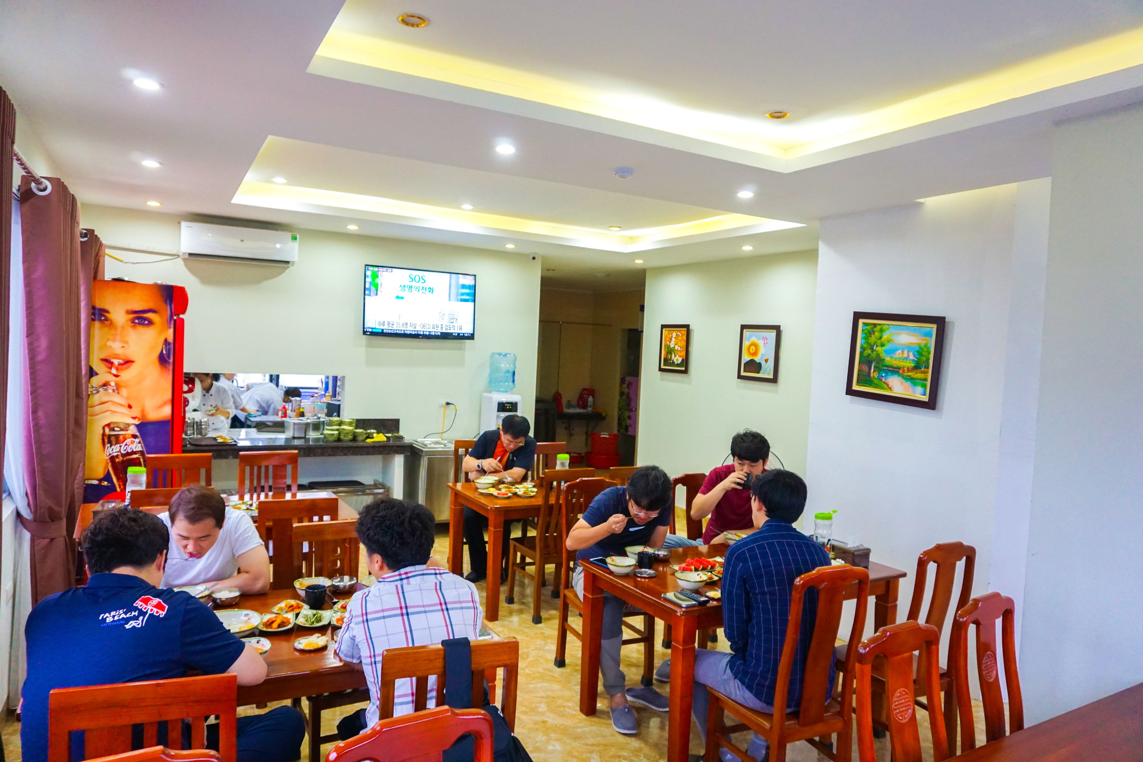 A dining area with multiple tables and chairs, a television screen, and a wall-mounted air conditioner.