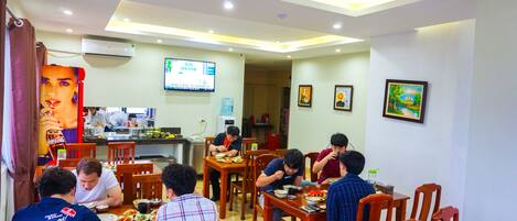 A dining area with multiple tables and chairs, a television screen, and a wall-mounted air conditioner.