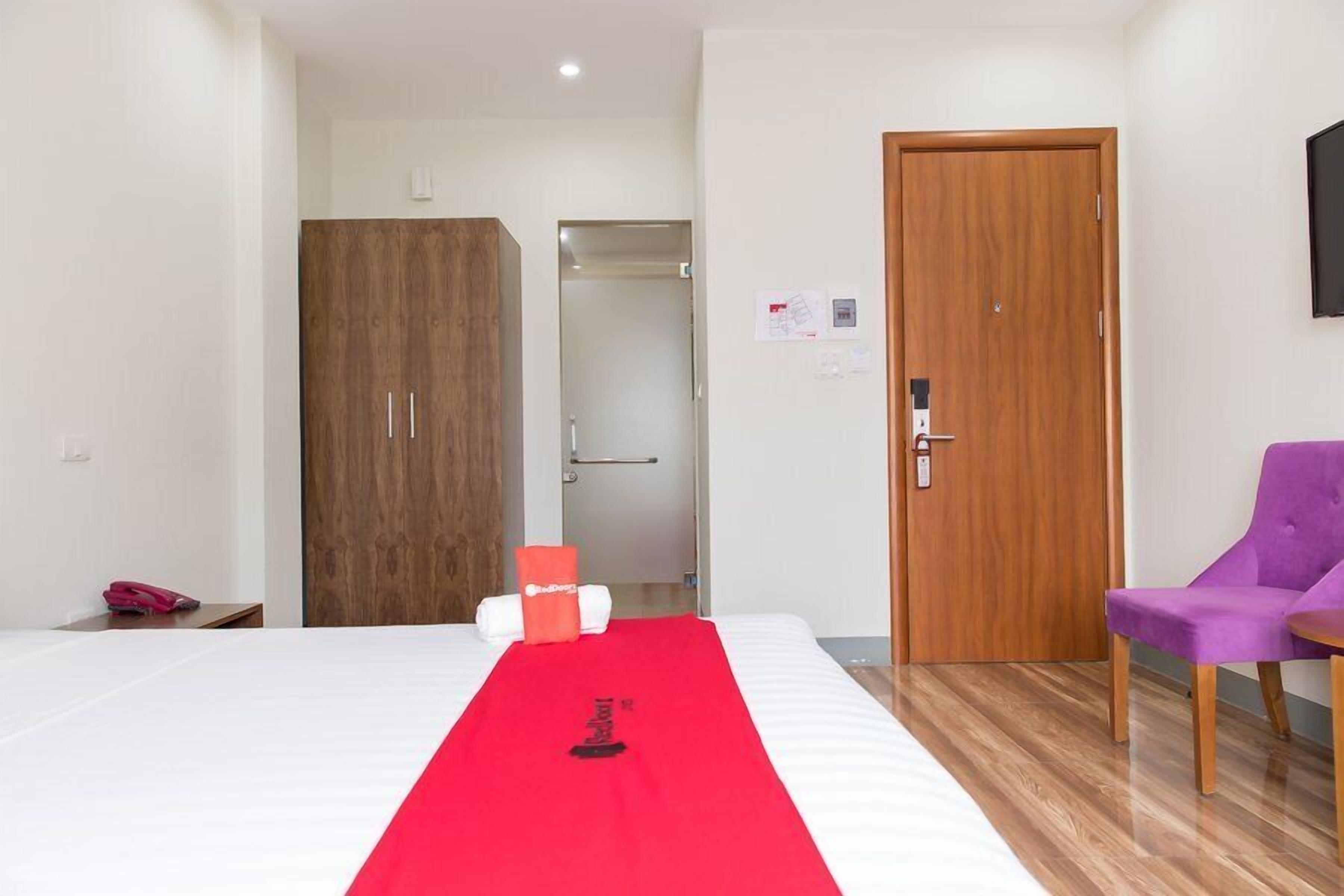 A hotel room with a bed, a red towel runner, a purple chair, and a wooden wardrobe.