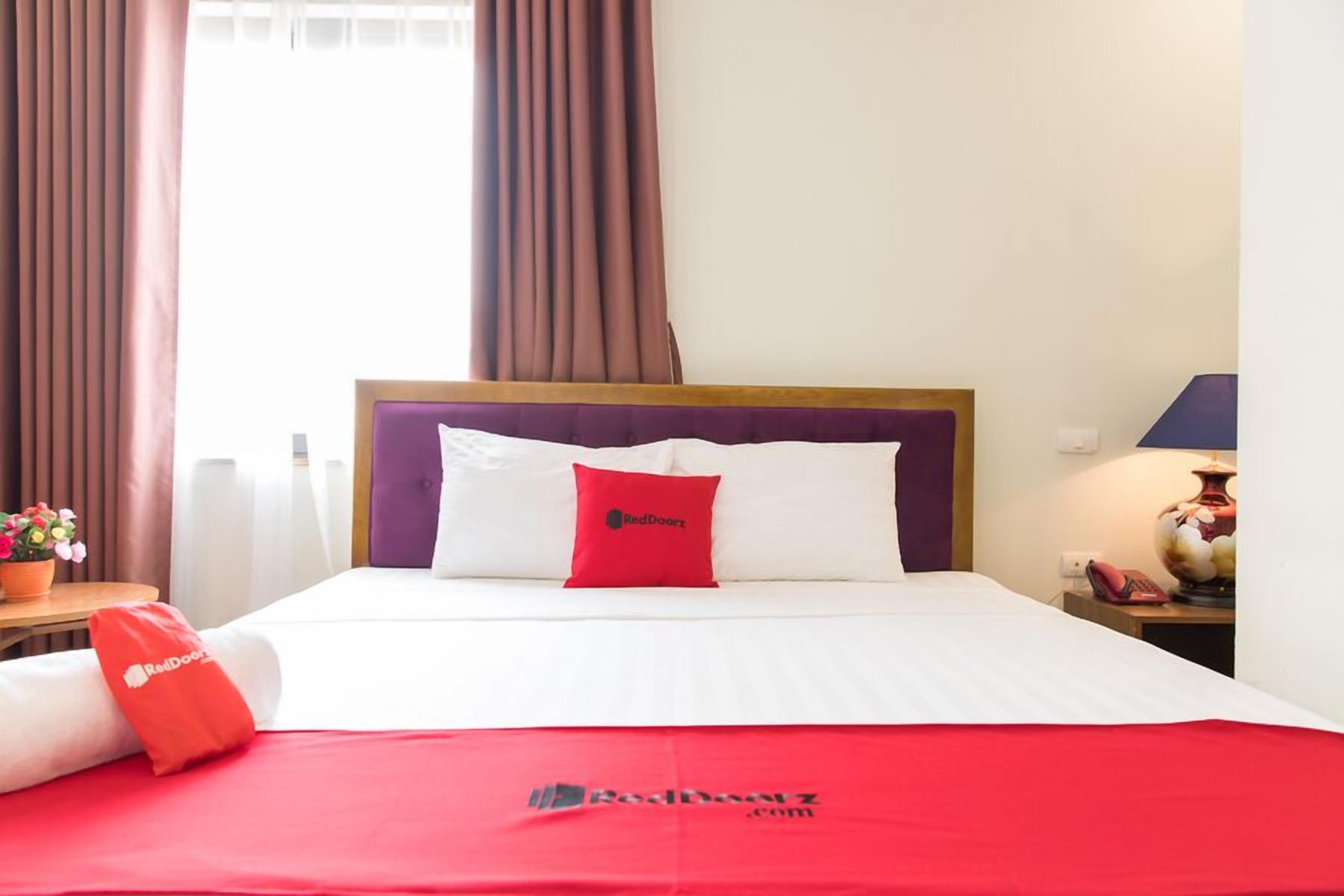A hotel room with a bed, a nightstand with a lamp, and a window with curtains.