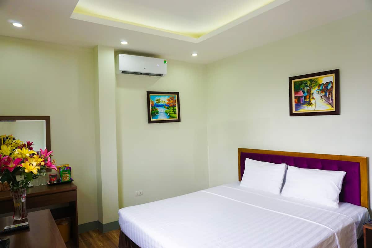Una habitación de hotel con una cama, un escritorio con un florero y dos cuadros en la pared.