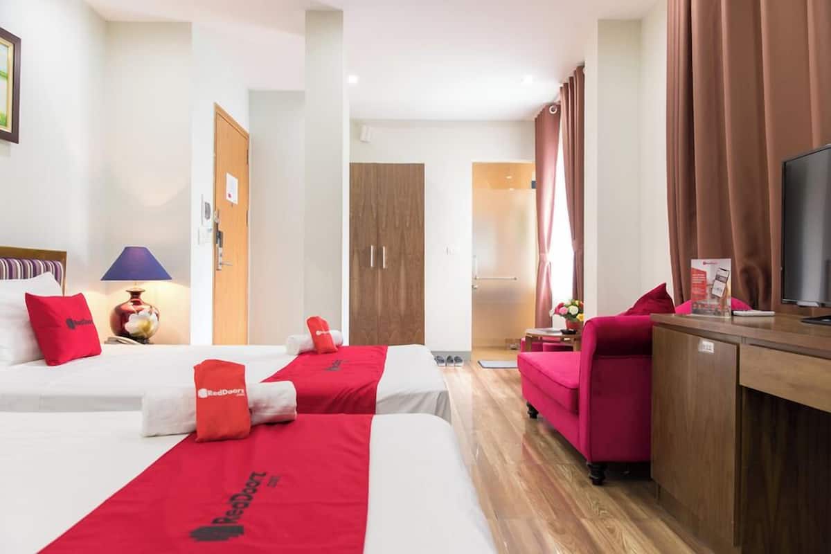 Habitación de hotel con dos camas, un escritorio, una silla y un televisor.