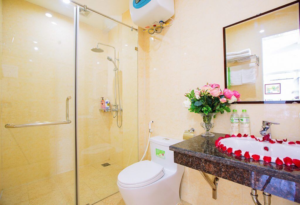A bathroom with a glass-enclosed shower, a white toilet, a sink with rose petals, and a mirror.