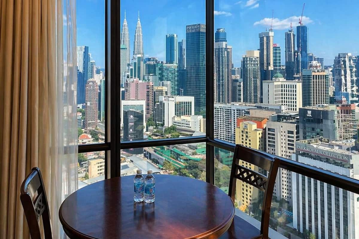 A room with a large window offering a city skyline view, a round wooden table with two water bottles, and a chair.