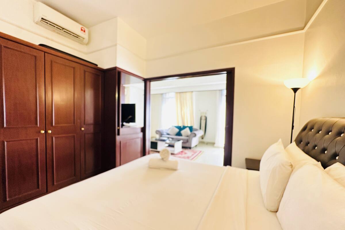 A hotel room with a large bed, a wardrobe, a flat-screen TV, and a lamp.