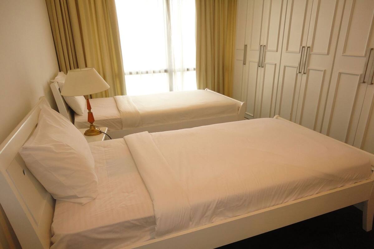 A hotel room with a single bed, a bedside table with a lamp, a window with curtains, and a wardrobe.