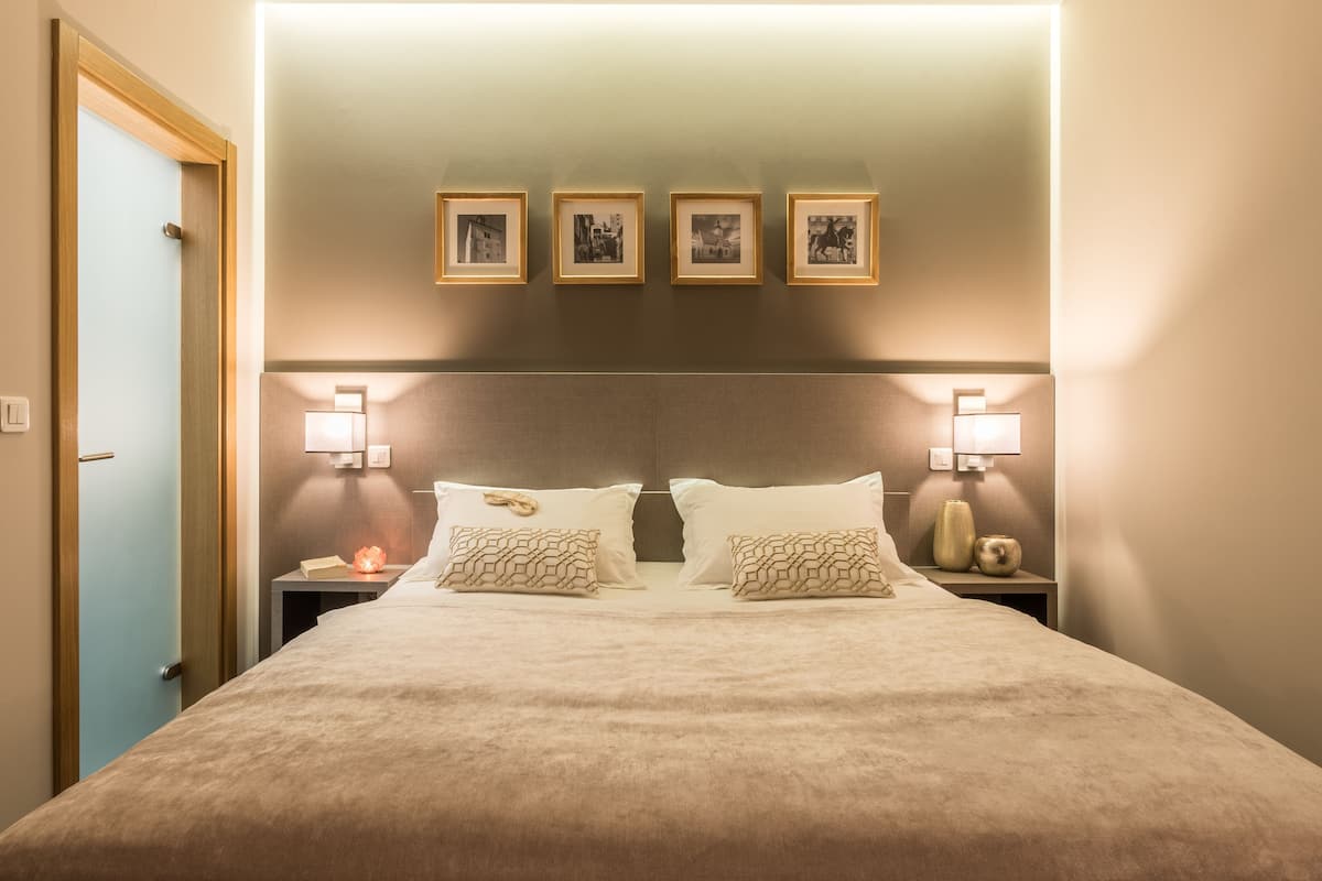 A hotel room with a large bed, two bedside tables, a nightstand, a wall-mounted light, and four framed pictures above the bed.