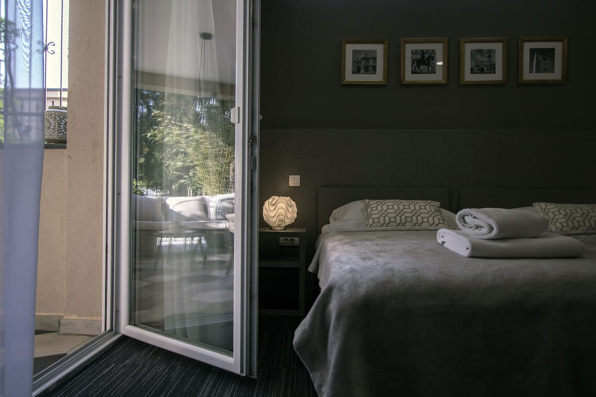 A hotel room with a bed, a nightstand, a lamp, and a view through a glass door.