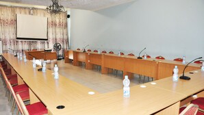 A conference room with a long table, red chairs, water bottles, and a projector screen.