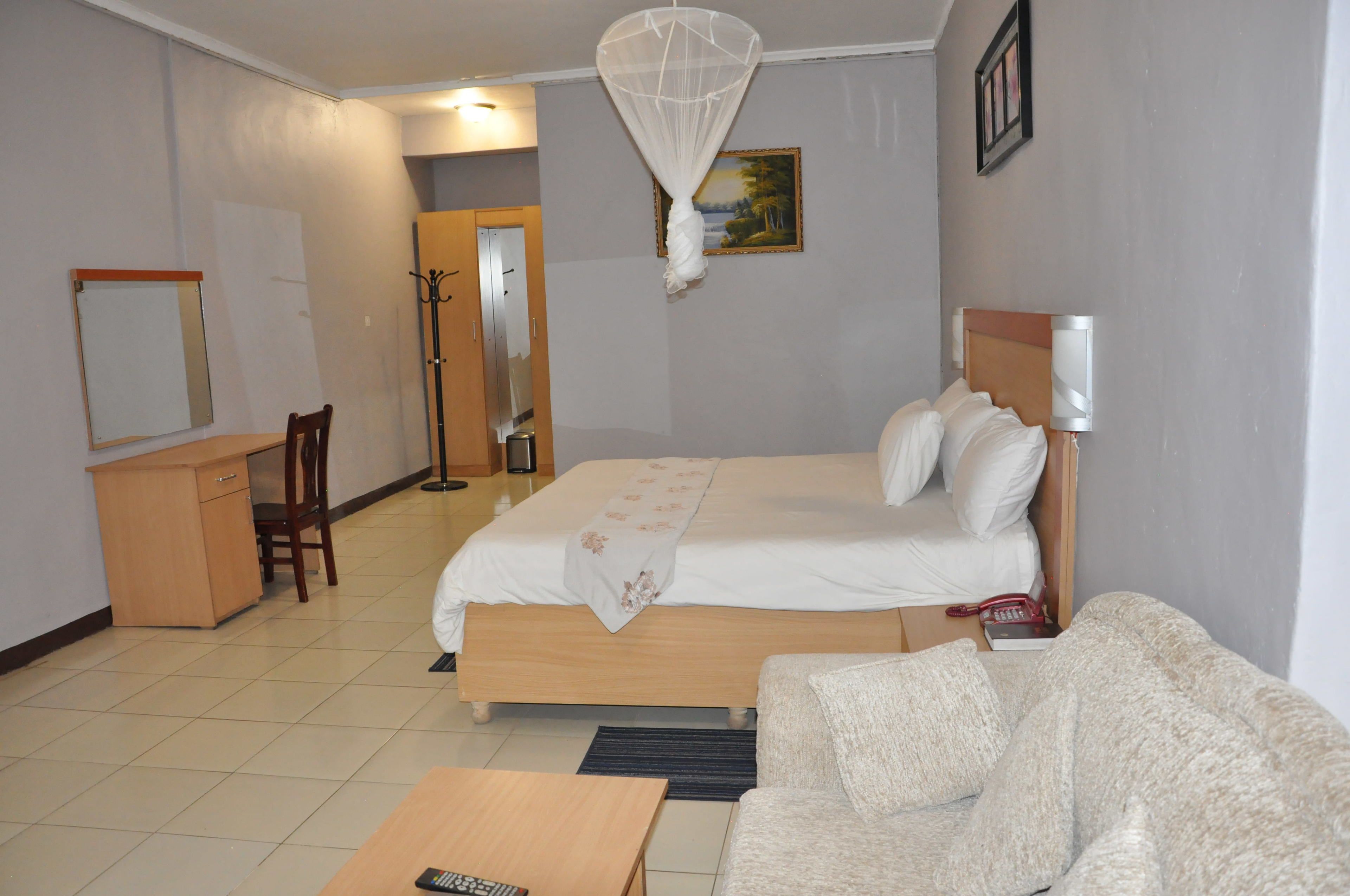 A hotel room with a bed, a desk, a chair, a sofa, and a bedside table.