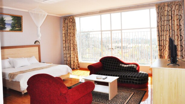 A hotel room with a bed, a red armchair, a white coffee table, and a large window with a view.