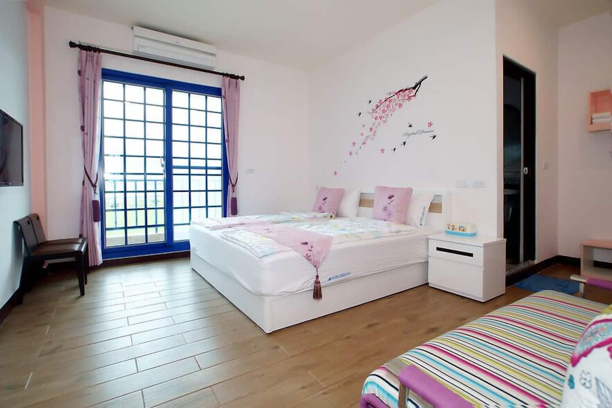 Une chambre à coucher comprenant un lit, des tables de chevet, un banc, une fenêtre avec des rideaux et un élément de décoration murale.