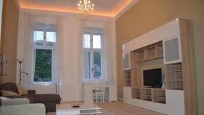 Un salon comprenant un canapé, une table basse, un meuble pour la télévision et de grandes fenêtres.