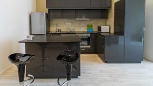 Une cuisine moderne avec des meubles de couleur sombre, un îlot central et deux tabourets de bar.