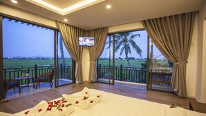 A hotel room with a large bed, a TV on the wall, and a balcony with a view of the countryside. - Hoi An Four Season Villa (Da Nang)