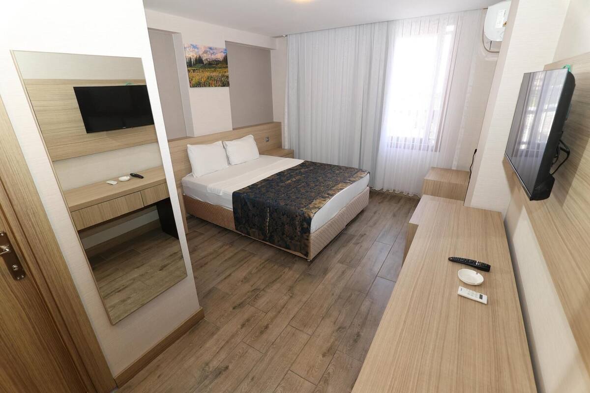 A hotel room with a bed, a desk, a television, and a window with curtains.