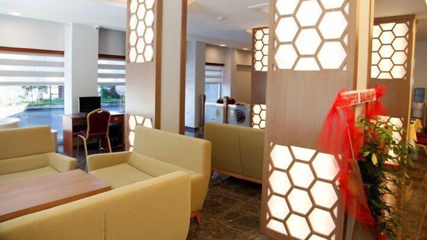 A hotel lobby with beige sofas, a reception desk, and hexagonal light panels. - Adana Omur Otel (Adana)