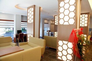 A hotel lobby with beige sofas, a reception desk, and hexagonal light panels. - Adana Omur Otel (Adana)