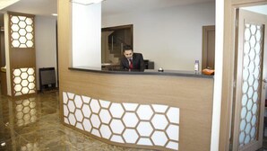 A reception desk with a hexagonal patterned design, a staircase in the background, and a polished floor. - Adana Omur Otel (Adana)