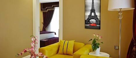 Una habitación con un sofá amarillo, un cuadro de la Torre Eiffel y una lámpara.