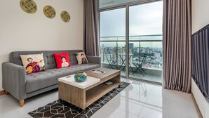 A modern living room with a grey sofa, decorative pillows, a wooden coffee table, and a large window offering a city view. - Hoasun Boutique Apartment - Vinhomes Central Park (Ho Chi Minh City)