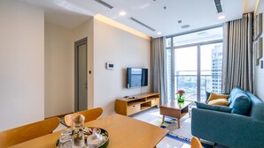 A modern hotel room with a dining area, a sofa, a TV, and a large window with a city view. - Hoasun Boutique Apartment - Vinhomes Central Park (Ho Chi Minh City)