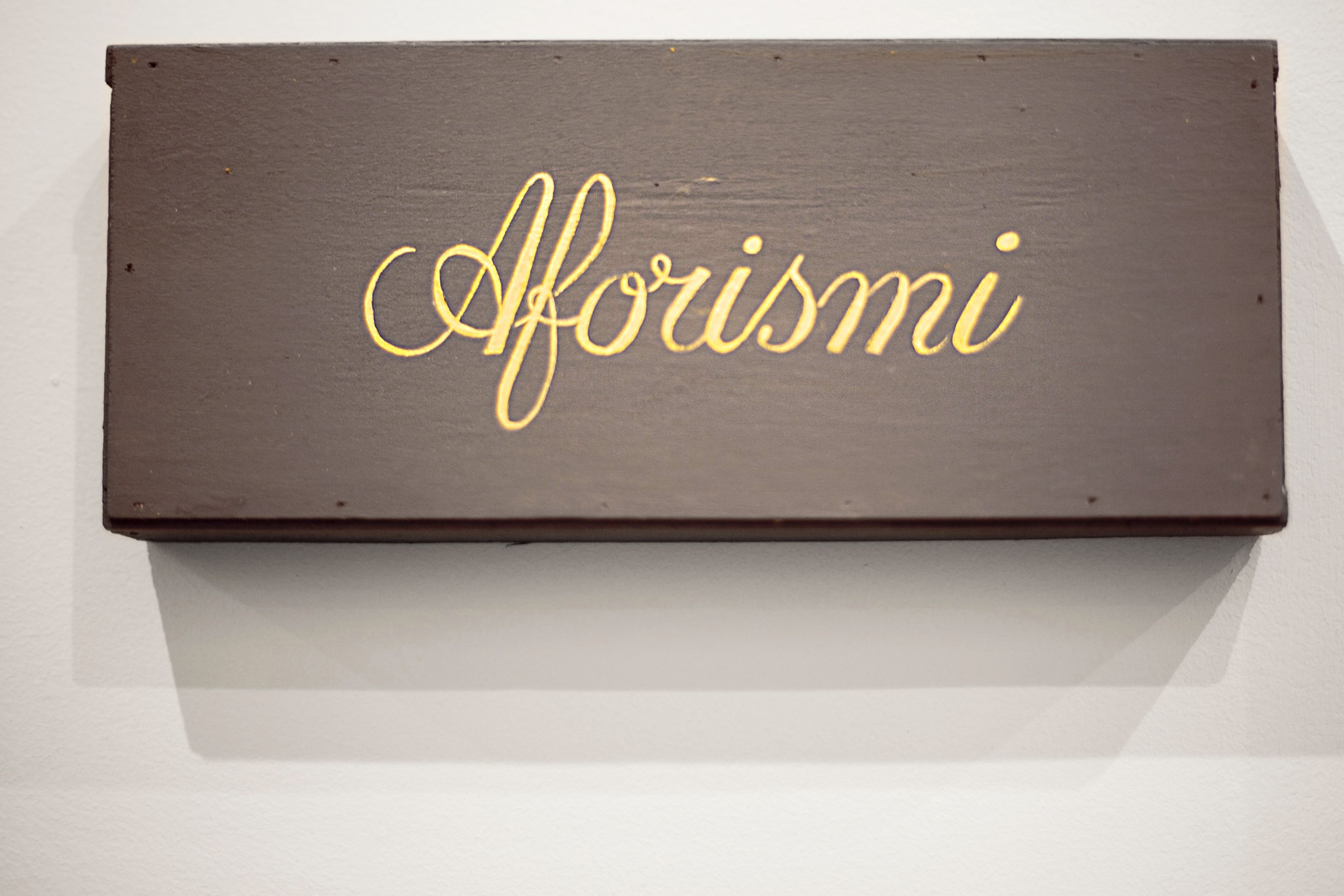 Tumma puinen kyltti, jossa sana ”Aforismi” on kirjoitettu kultaisin kirjaimin.