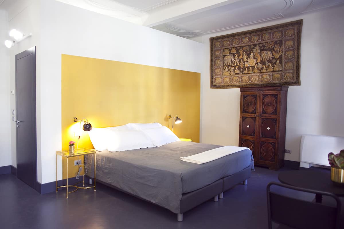 A hotel room with a bed, bedside lamps, a wooden cabinet, and a wall-mounted artwork.