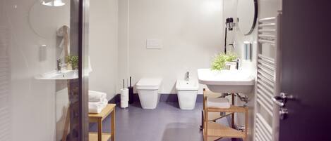 Et moderne badeværelse med glasvæg, vask, toilet og spejl.