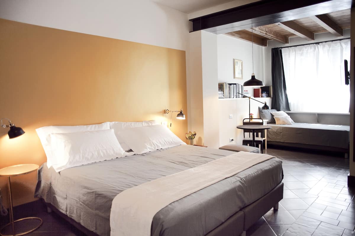 A hotel room with a bed, bedside table, lamp, and a window with curtains.