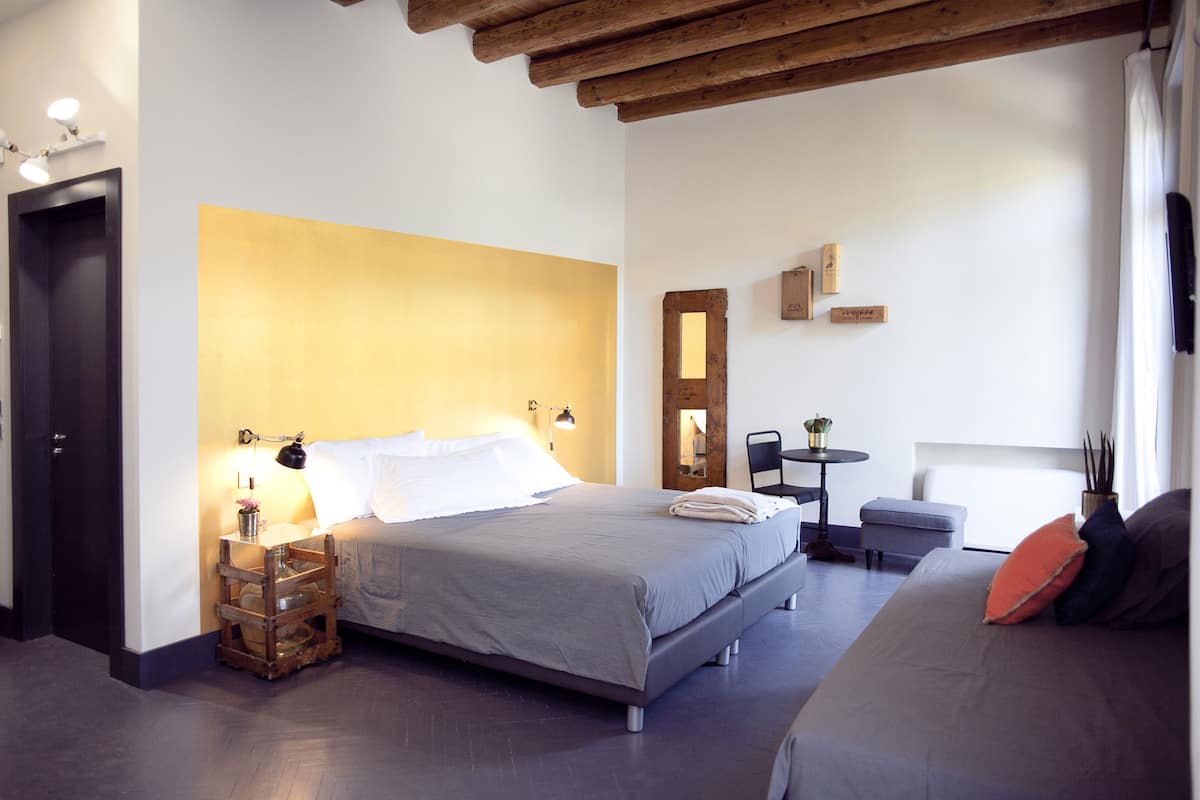 A bedroom with a bed, bedside table, lamp, and a small table with a plant.