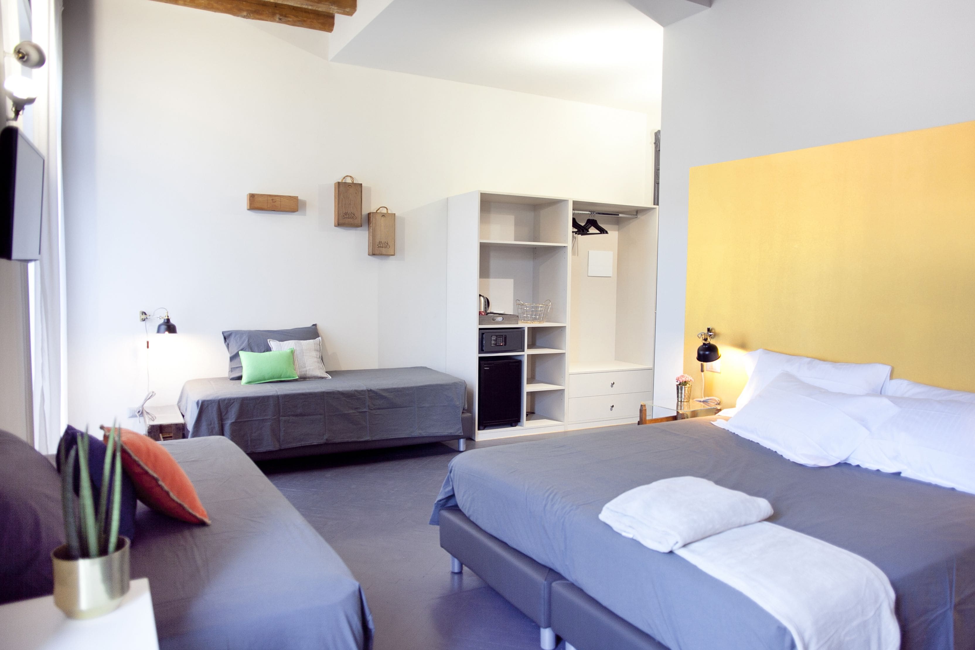 A hotel room with two beds, a wardrobe, and a desk with a lamp.