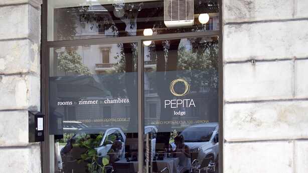 A hotel entrance with a glass door, a metal decorative arch, and a sign indicating it is a PEPITA lodge. - Pepita Lodge (Verona)