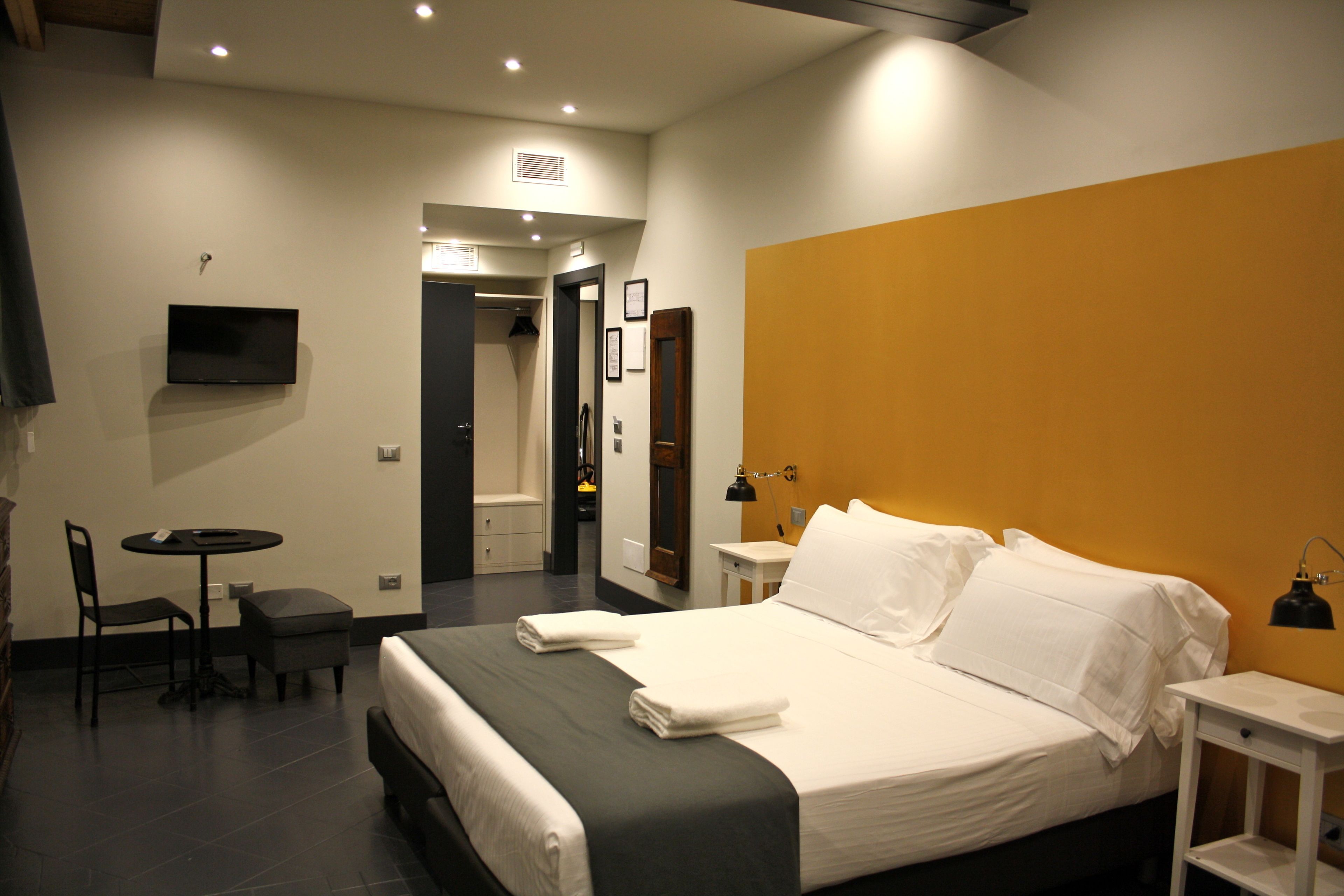 Una camera d'albergo con un letto, una scrivania, una sedia, una TV e un bagno visibile attraverso una porta aperta.