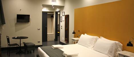 Una camera d'albergo con un letto, una scrivania, una sedia, una TV e un bagno visibile attraverso una porta aperta.