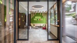 A modern hotel lobby with a green wall, wooden accents, and a seating area with a table and chairs. - Hotel Val di Sole (Mezzana)