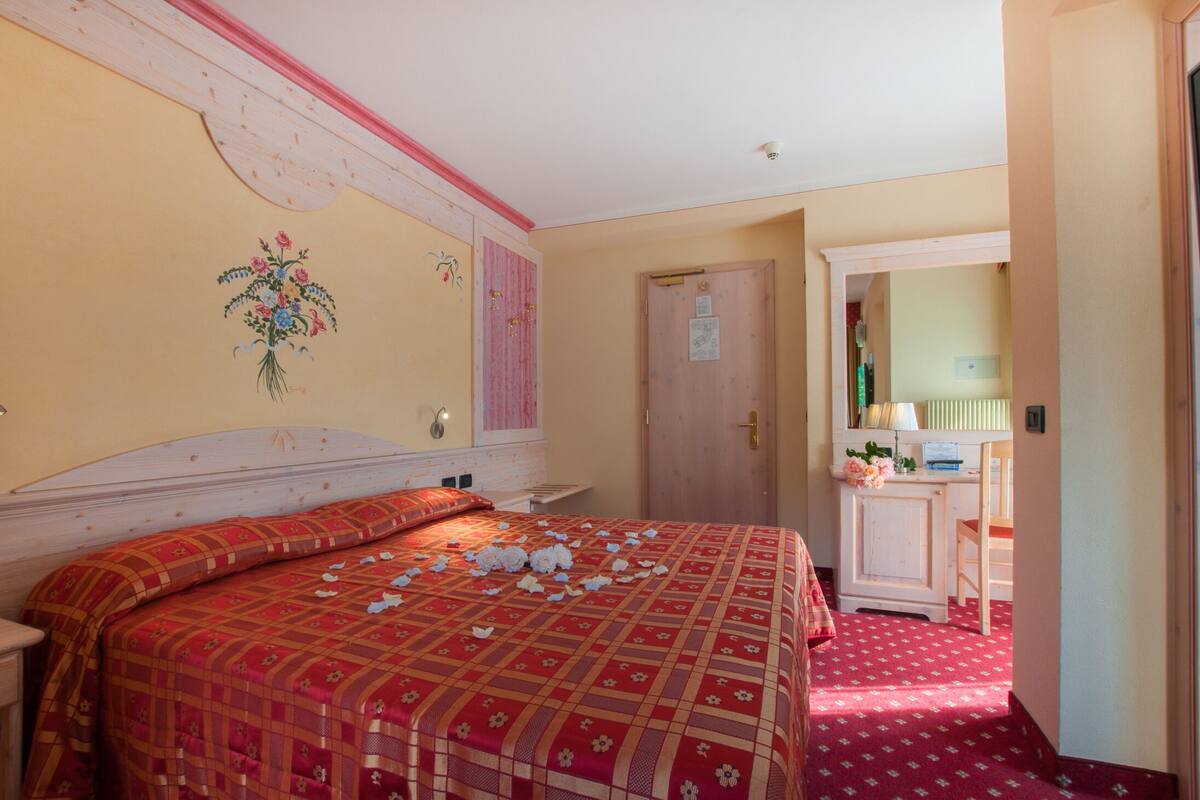 A bedroom with a large bed, a wooden headboard, a door with a mirror, and a small desk with a chair.