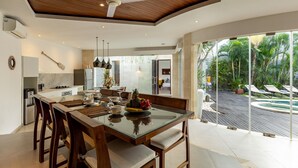 A modern kitchen with a dining area, large windows, and a ceiling fan.